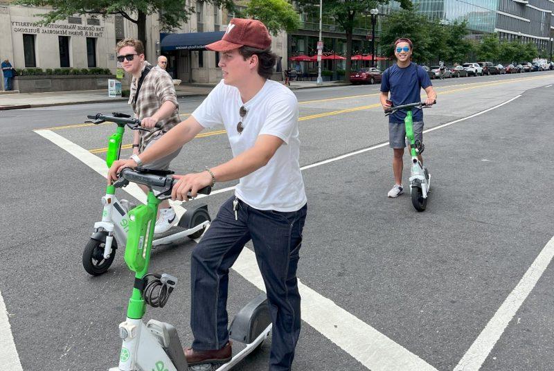 Students riding e-scooters pause on a city street. 